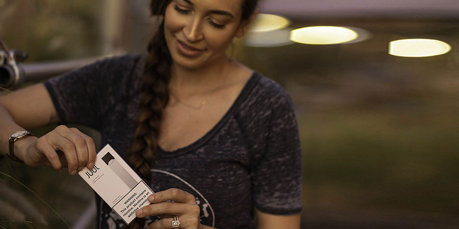 a woman with long braided hair holding a merch box of a vape device